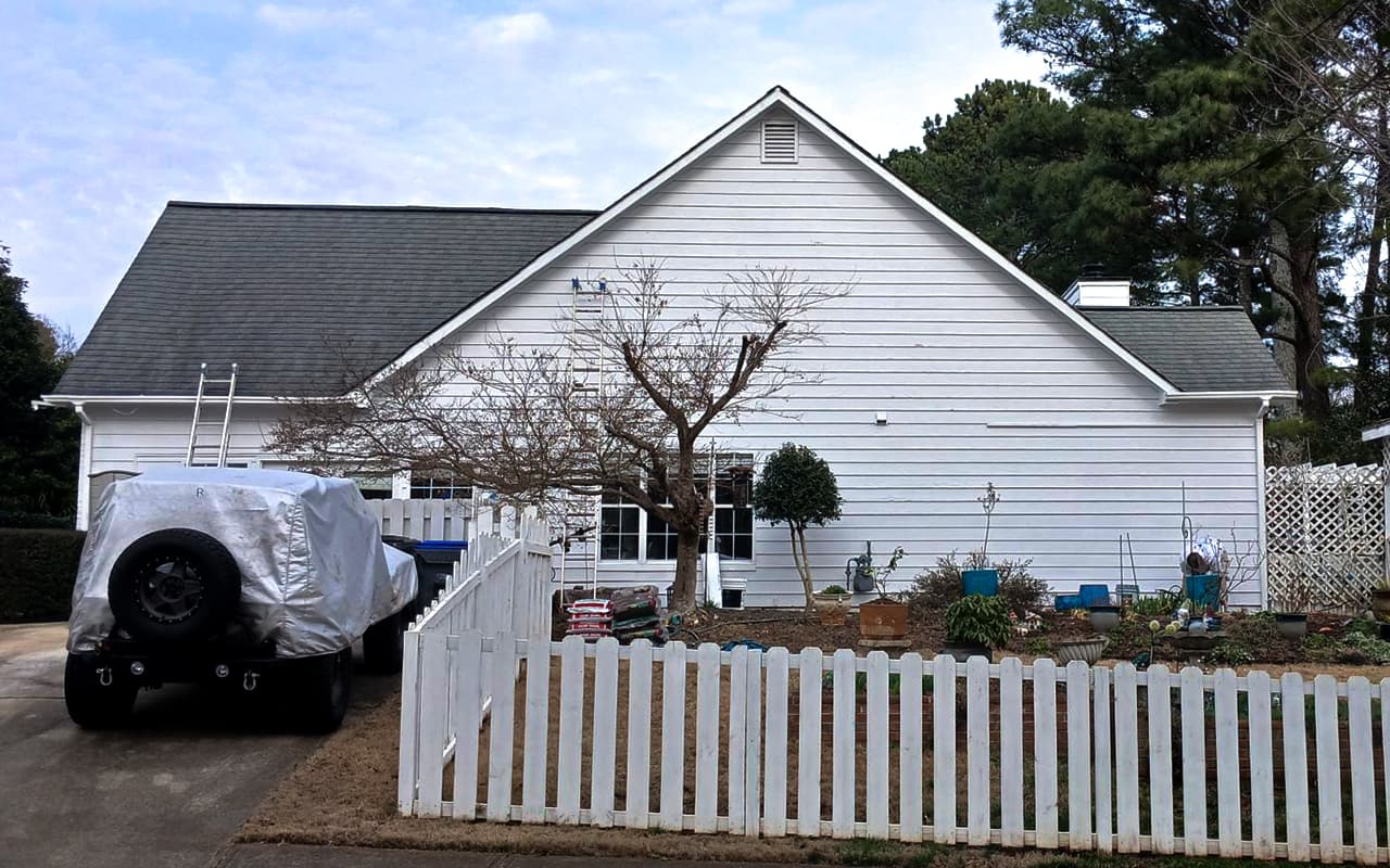 Exterior painting project with a nearby vehicle fully covered to protect it from overspray, debris, and paint.